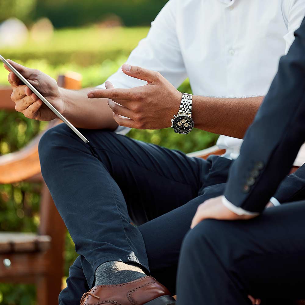 man wearing watch and pointing at ipad with man in suit beside him