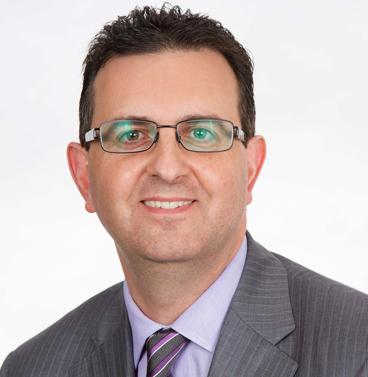 smiling man with short brown hair and glasses wearing grey suit and striped grey and purple tie