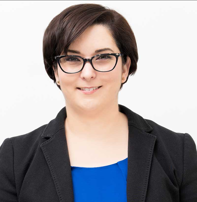 smiling woman with short brown hair and glasses wearing black blazer and blue shirt