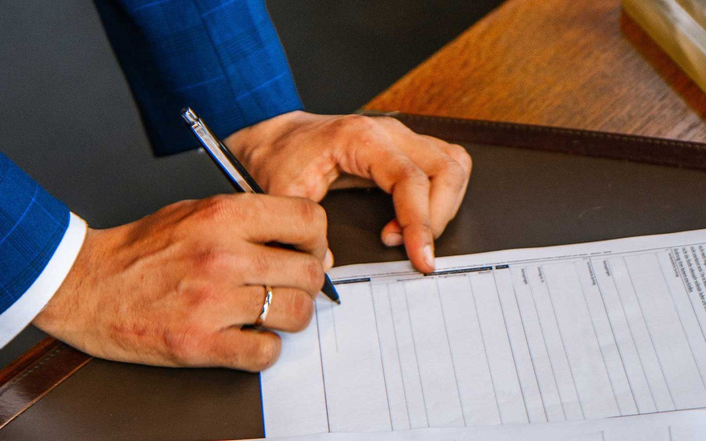 arm of man in blue suit holding pen writing on paper