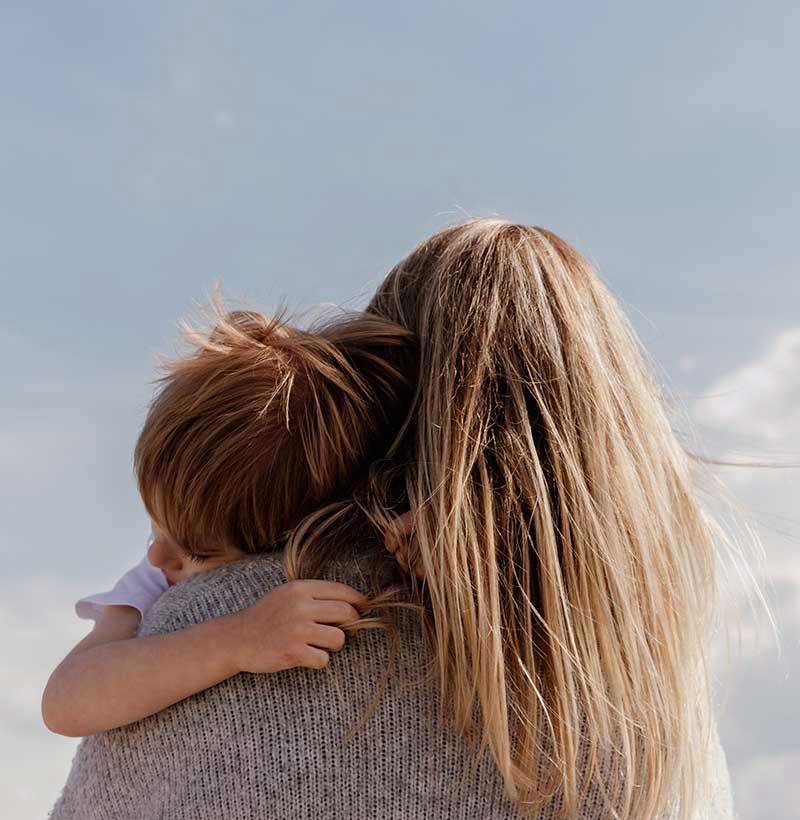 back of woman with long dirty blonde hair holding son