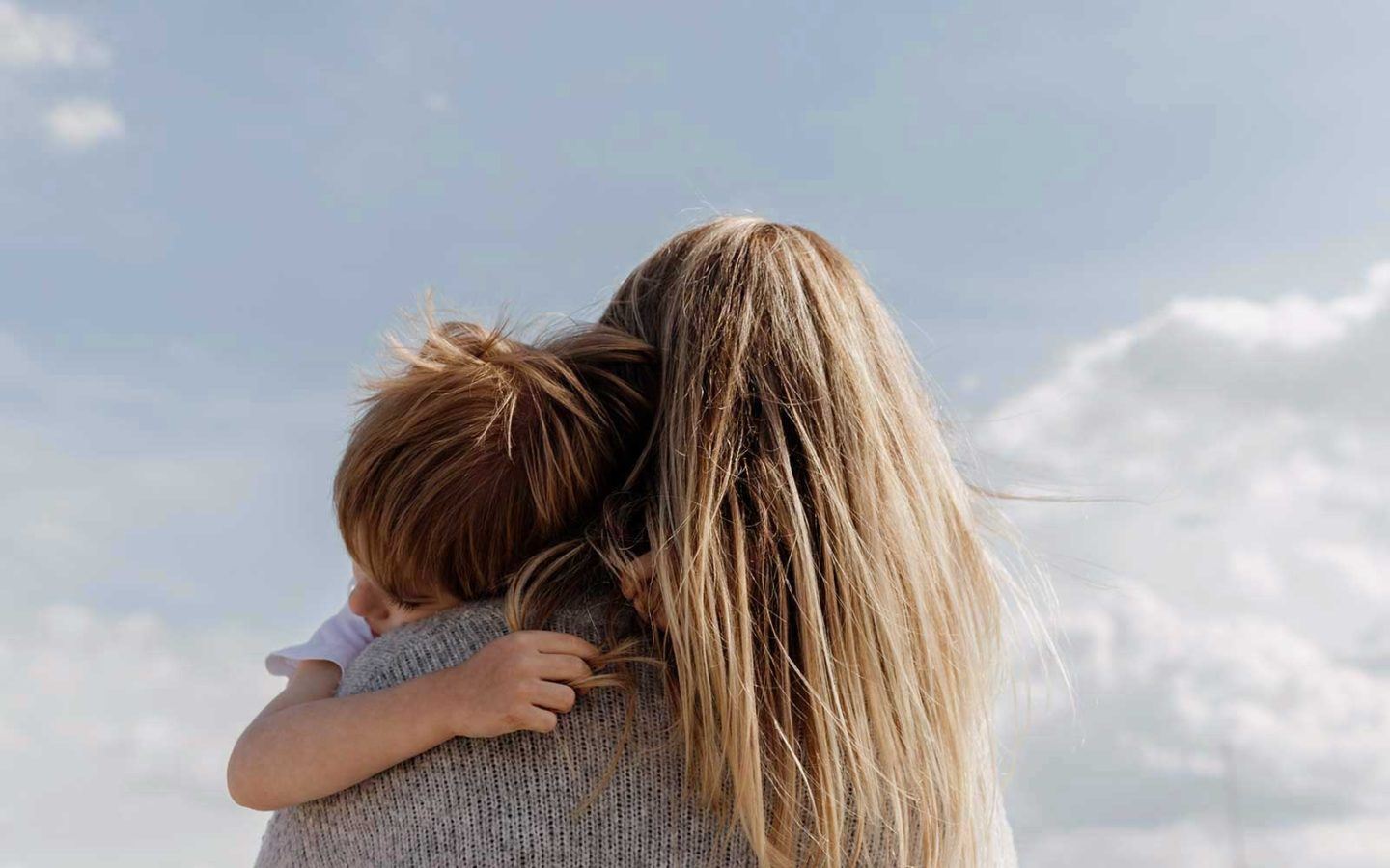 back of woman with long dirty blonde hair holding son